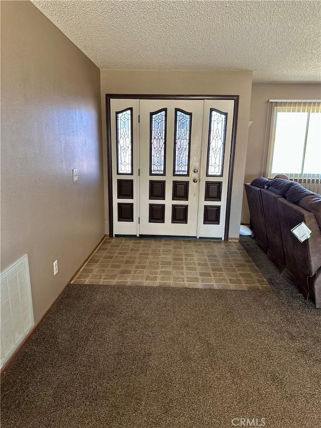 foyer with carpet, visible vents, vaulted ceiling, and a textured ceiling