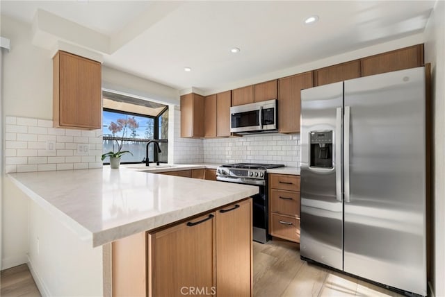 kitchen featuring a peninsula, a sink, appliances with stainless steel finishes, decorative backsplash, and light wood finished floors