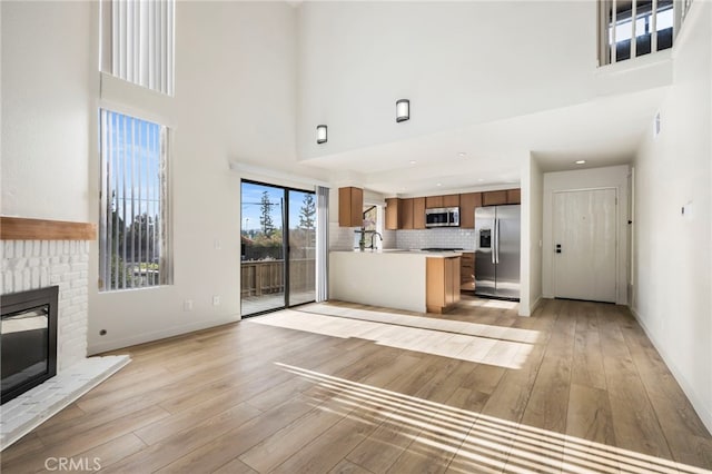 unfurnished living room with a brick fireplace, light wood-style flooring, and a high ceiling