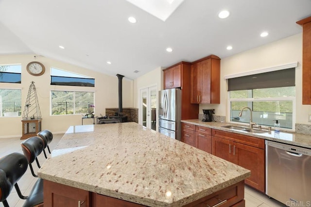 kitchen featuring light stone countertops, lofted ceiling with skylight, appliances with stainless steel finishes, a wood stove, and a sink