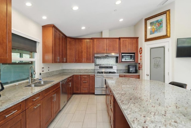 kitchen featuring light stone countertops, under cabinet range hood, lofted ceiling, appliances with stainless steel finishes, and a sink