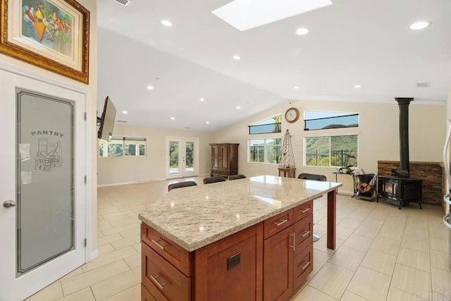 kitchen with light stone countertops, a kitchen island, open floor plan, lofted ceiling with skylight, and brown cabinets