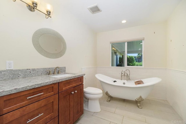 full bath with a freestanding tub, visible vents, vanity, and wainscoting