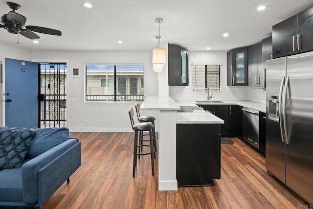 kitchen with a breakfast bar, stainless steel appliances, glass insert cabinets, dark cabinetry, and a peninsula