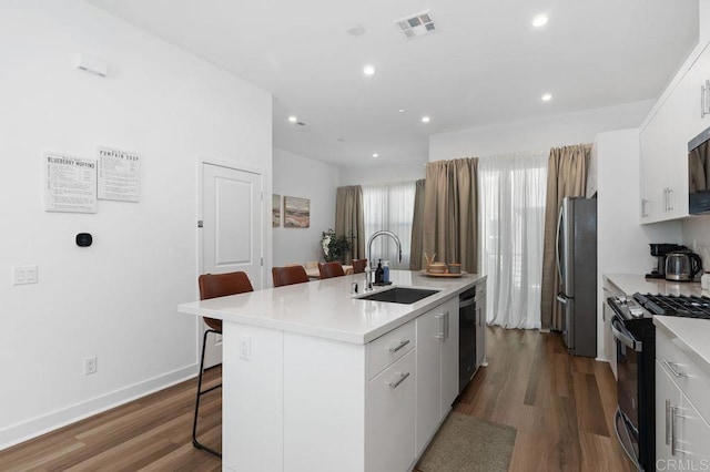 kitchen featuring a center island with sink, visible vents, black range with gas stovetop, freestanding refrigerator, and a sink