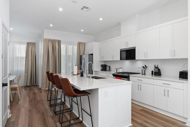 kitchen with a breakfast bar, a center island with sink, stainless steel appliances, visible vents, and a sink