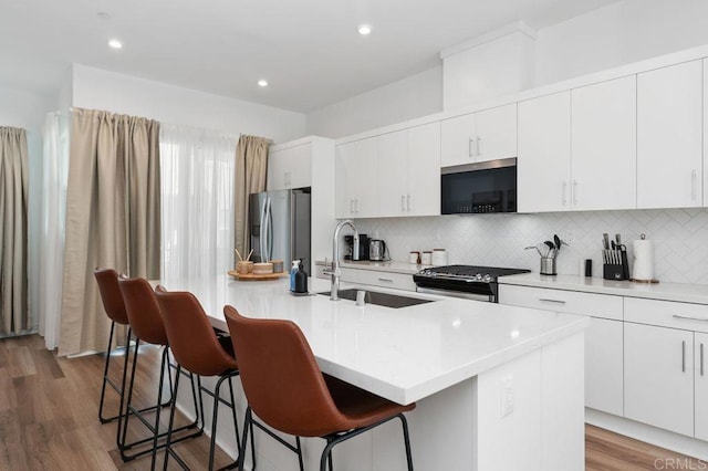 kitchen with a breakfast bar area, appliances with stainless steel finishes, light wood-style floors, a sink, and an island with sink