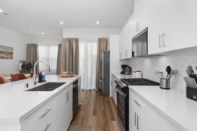 kitchen with wood finished floors, a sink, white cabinets, appliances with stainless steel finishes, and an island with sink