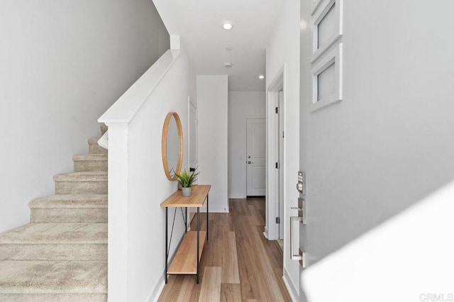 hallway featuring baseboards, stairway, wood finished floors, and recessed lighting