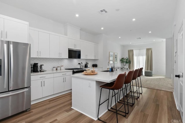 kitchen with visible vents, decorative backsplash, appliances with stainless steel finishes, a kitchen bar, and a sink