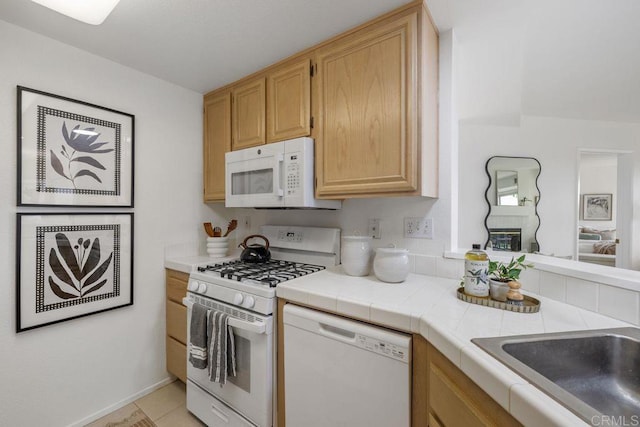 kitchen with white appliances, a sink, tile countertops, and light brown cabinetry