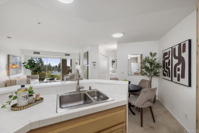 kitchen featuring light carpet, a sink, visible vents, open floor plan, and tile counters