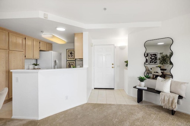 kitchen with light tile patterned floors, light brown cabinets, light colored carpet, white refrigerator with ice dispenser, and light countertops