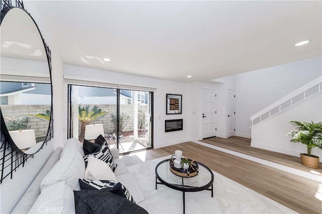 living room featuring recessed lighting, a glass covered fireplace, wood finished floors, baseboards, and stairs