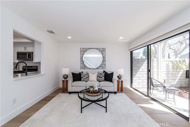 living room featuring light wood-type flooring, visible vents, baseboards, and recessed lighting