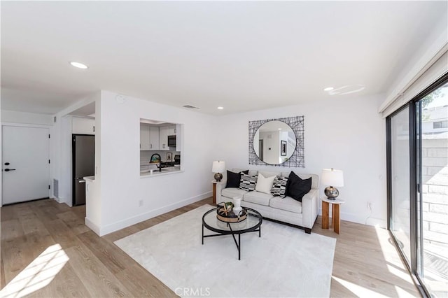 living room featuring light wood-style floors, visible vents, baseboards, and recessed lighting