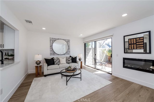 living area featuring recessed lighting, wood finished floors, visible vents, baseboards, and a glass covered fireplace