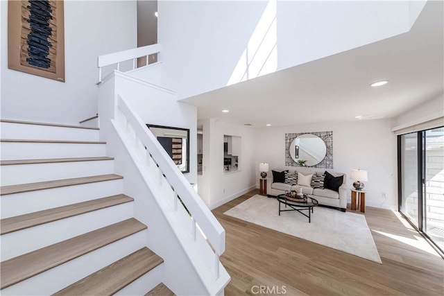 stairs with a high ceiling, wood finished floors, and recessed lighting