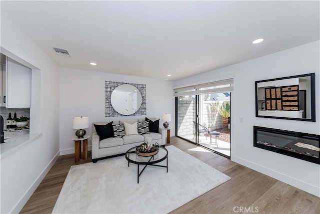 living area with light wood finished floors, recessed lighting, visible vents, a glass covered fireplace, and baseboards