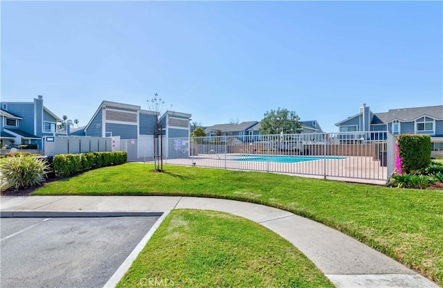 community pool with a residential view, fence, and a lawn