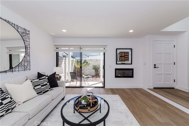 living room featuring a glass covered fireplace, recessed lighting, wood finished floors, and baseboards