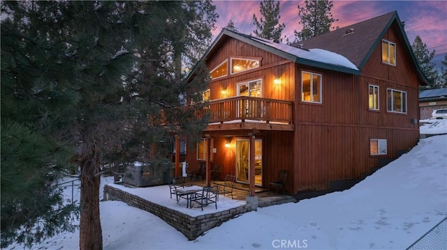 snow covered rear of property featuring a deck and a patio