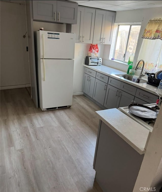 kitchen featuring gray cabinets, light wood-type flooring, freestanding refrigerator, and a sink