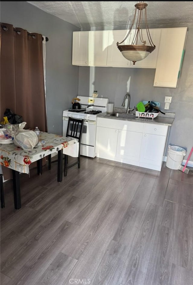 kitchen featuring a sink, white gas stove, dark wood finished floors, and white cabinetry