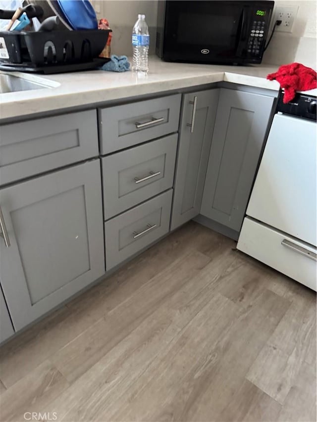 kitchen with light wood finished floors, black microwave, light countertops, gray cabinets, and range