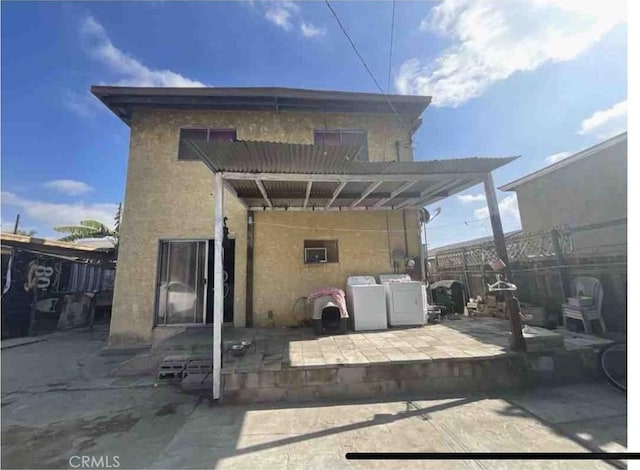 rear view of house featuring washer and dryer, stucco siding, fence, and a patio area