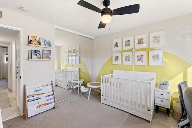 carpeted bedroom with tile patterned flooring, a nursery area, a ceiling fan, and a closet