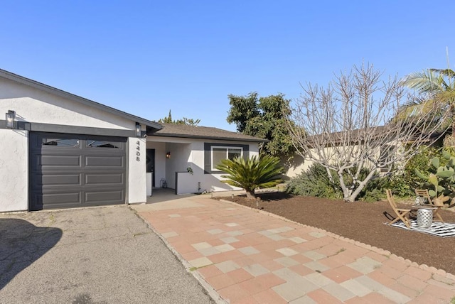 ranch-style house with stucco siding, an attached garage, and aphalt driveway