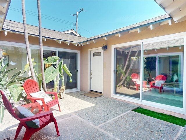 view of exterior entry featuring a patio area, a shingled roof, and stucco siding