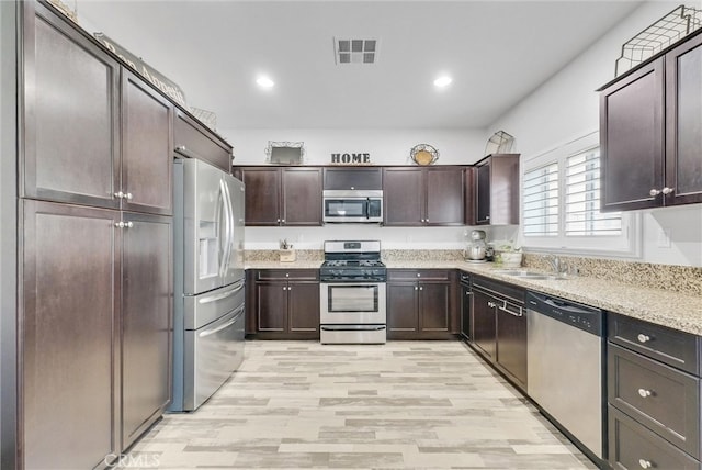 kitchen with light stone counters, a sink, visible vents, dark brown cabinets, and appliances with stainless steel finishes