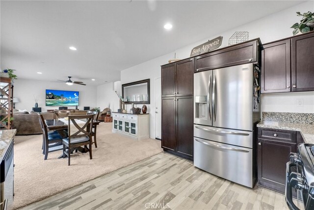 kitchen featuring light stone counters, dark brown cabinetry, open floor plan, stainless steel refrigerator with ice dispenser, and gas range