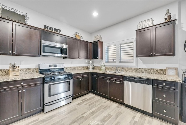 kitchen featuring light stone counters, light wood finished floors, appliances with stainless steel finishes, dark brown cabinetry, and a sink