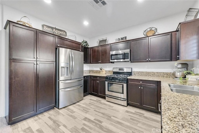 kitchen with light stone counters, visible vents, dark brown cabinets, appliances with stainless steel finishes, and light wood-type flooring