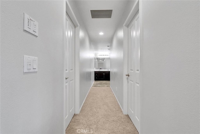 corridor with light carpet, a textured wall, visible vents, and baseboards