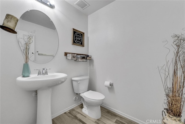 bathroom featuring toilet, a sink, wood finished floors, visible vents, and baseboards