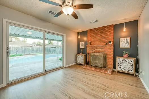 unfurnished living room featuring a textured ceiling, a fireplace, wood finished floors, visible vents, and baseboards