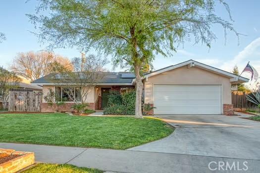 single story home featuring driveway, a front lawn, solar panels, and fence