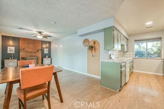 kitchen featuring tile countertops, a textured ceiling, a fireplace, light wood-style floors, and green cabinetry