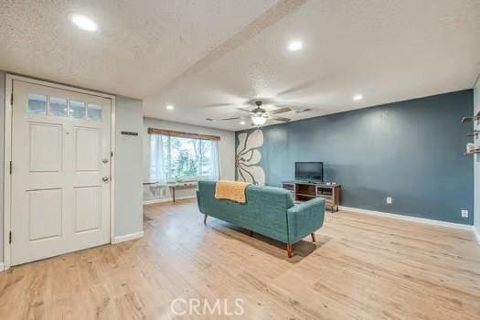 living area featuring a ceiling fan, a textured ceiling, baseboards, and wood finished floors