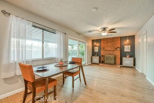 dining space with a textured ceiling, ceiling fan, baseboards, light wood-style floors, and a brick fireplace