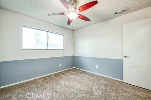 carpeted spare room featuring baseboards, ceiling fan, visible vents, and a textured ceiling