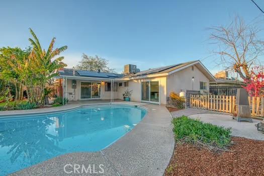 rear view of house featuring a patio area, roof mounted solar panels, fence, and a fenced in pool