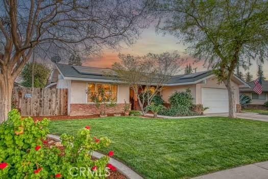 single story home featuring driveway, a garage, solar panels, fence, and a front yard