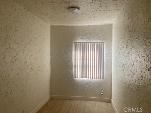 spare room with a textured wall, baseboards, and wood finished floors