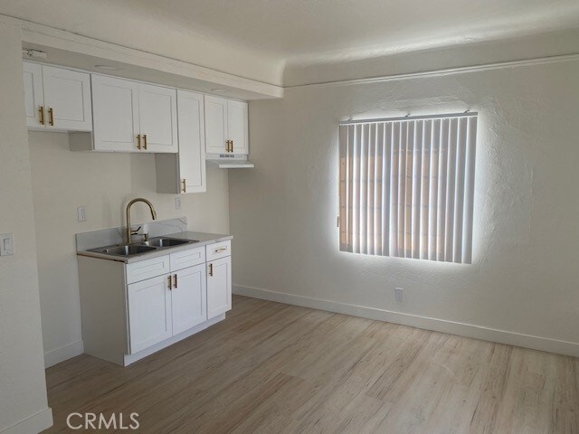 kitchen featuring baseboards, a sink, light wood-style flooring, and white cabinets