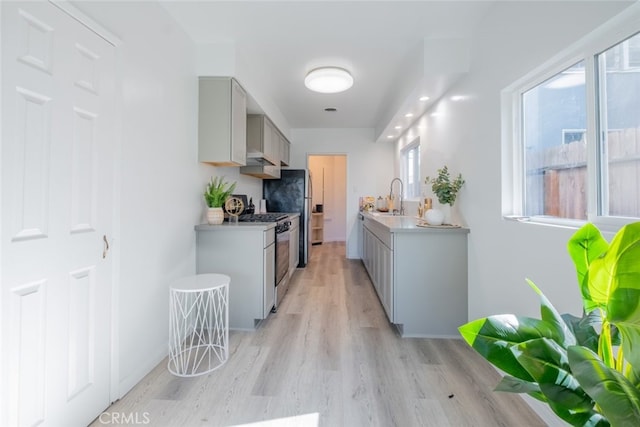 kitchen with range with gas cooktop, gray cabinets, light countertops, light wood-style floors, and a sink